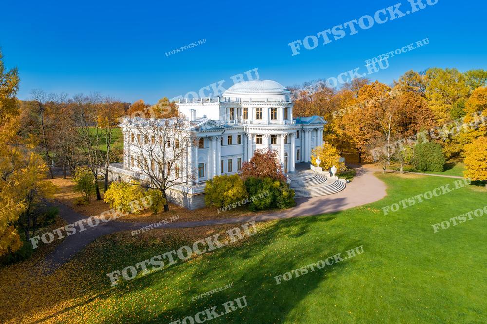 Эта фотография показывает дворец на Елагином острове в Санкт-Петербурге во всей красе золотой осени. Дворец, окружённый парком с разноцветной листвой, выделяется своей элегантностью и гармонично вписывается в природный ландшафт.